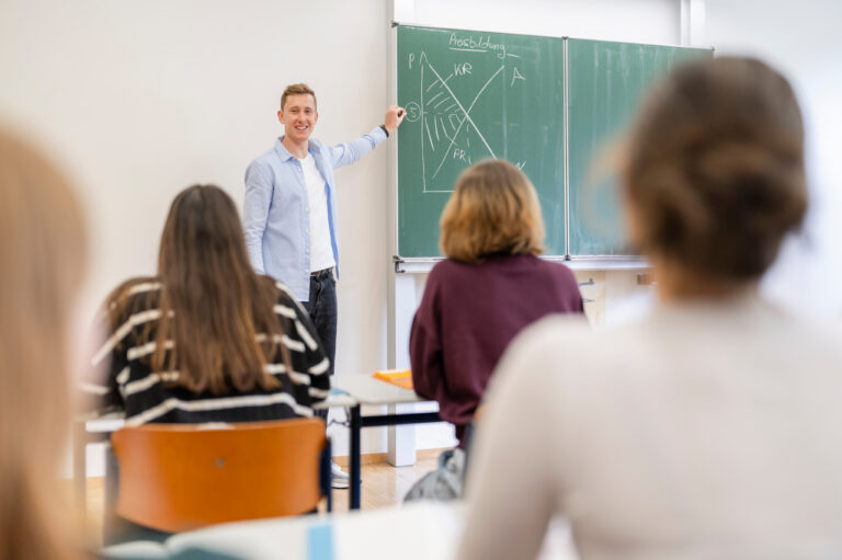 Lehrer an der Tafel vor Schuelerinnen.jpg